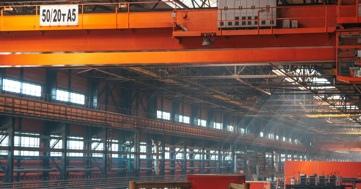 Spacious factory interior featuring large overhead cranes and metal walkways.