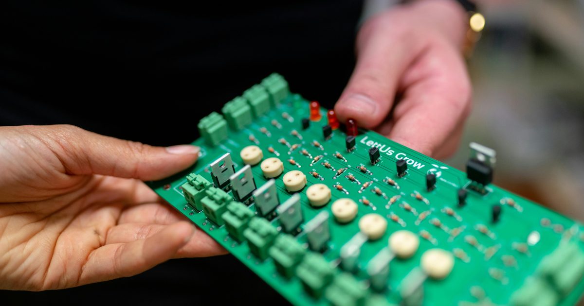 Close-up of hands holding a green circuit board used for electronic projects.