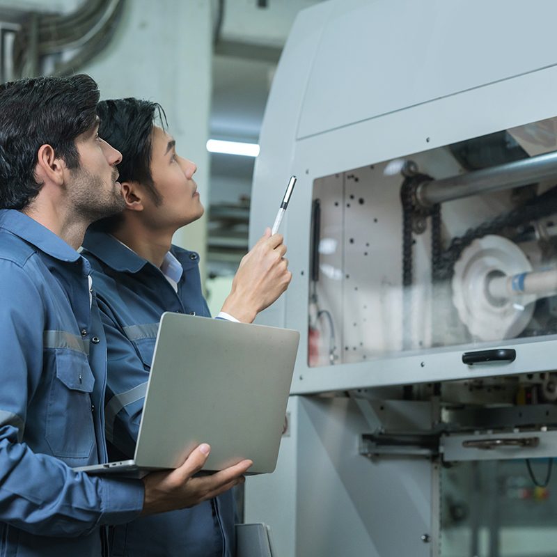 Male Asian caucasian engineer professional having a discussion standing consult at machine in the factory ,two expert coworker brainstorm explaining and solves the process of the cnc operate machine