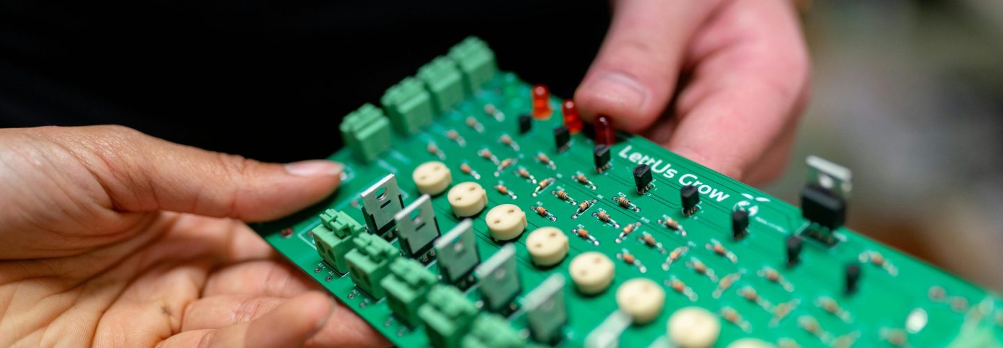 Close-up of hands holding a green circuit board used for electronic projects.